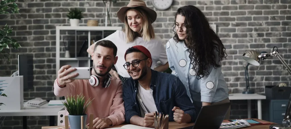 Two male and two female employees taking selfies in an office