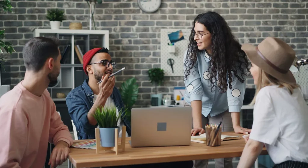 A diverse creative team of four people collaborating around a wooden desk in a modern office.
