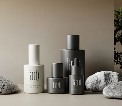 Minimalist skincare bottles in neutral gray and white packaging arranged with smooth stones and greenery on a beige background, creating a calm, modern aesthetic.